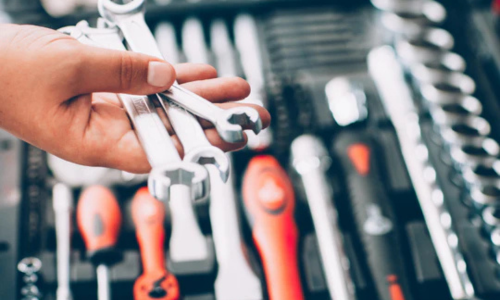 A hand holding wrenches above a socket set in the background